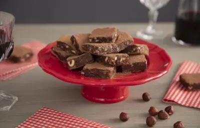 Fotografía en tonos rojos sobre un banco de madera clara con telas a cuadros rojos. En el centro, un puesto de tarta roja con dulces de chocolate trufados.