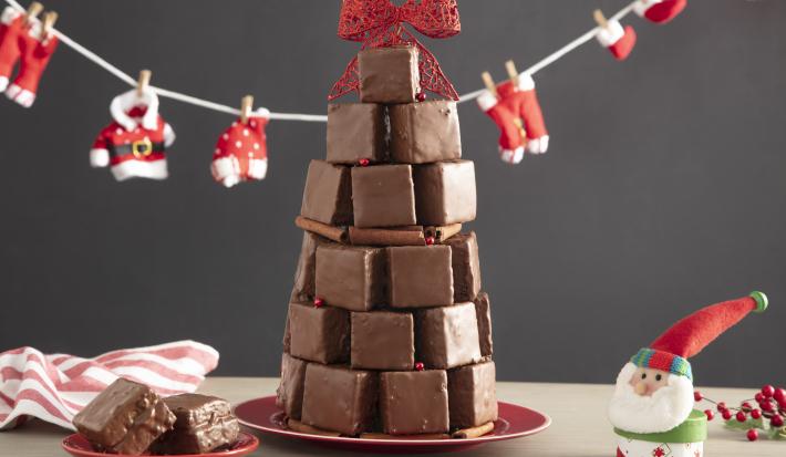 Fotografía en tonos rojos sobre un banco de madera con un pequeño tendedero de Papá Noel, un adorno de Papá Noel en el lado derecho, un plato pequeño con dos bollos y en el centro varios bollos formando un árbol de Navidad.